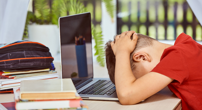 A boy putting his hands over his head because he is sad and in front of him is an opened laptop.