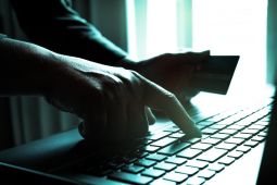 رجل يستخدم حاسوبًا محمولًا ويحمل بطاقة ائتمانية.