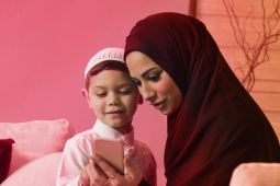 أم عربية مع ابنها الصغير يستخدمان هاتفًا محمولًا.