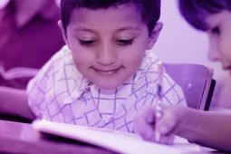 A young student catching a glimpse of his friend’s notebook while they’re in the classroom.