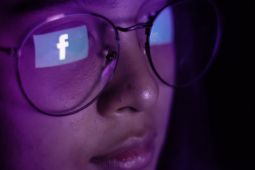 A teenage girl wearing glasses with the facebook logo reflected on them.