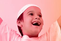 A young boy smiling and raising his hands high. 