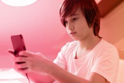A young boy wearing a white t-shirt and looking at his smartphone.
