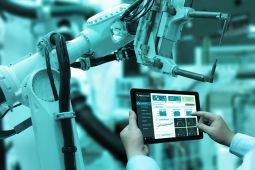 Hands holding a tablet to control a robot in a factory.