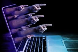 Representation of cyberbullying where hands coming out from a laptop and are pointing out.
