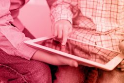 Hands of a kid putting a finger on a tablet while the older kid is holding it.