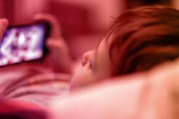 طفل مستلقي يشاهد مقطع فيديو على هاتف محمول.