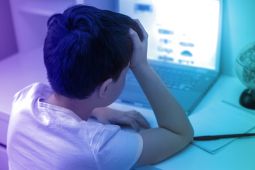 A young boy looking at the laptop screen, and has his head on his hand.
