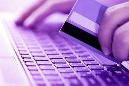 A hand holding a credit/debit card and the other hand is typing on the keyboard of a laptop.