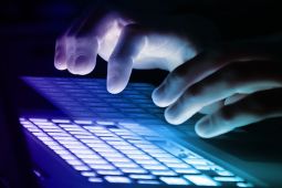 Hands typing on a keyboard and the background is dark.