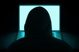 صورة تُظهر ظهر رجل يرتدي قميص ذات غطاء أسودة لأنه يمثل المُتسلل وأمامه جهاز كمبيوتر محمول.